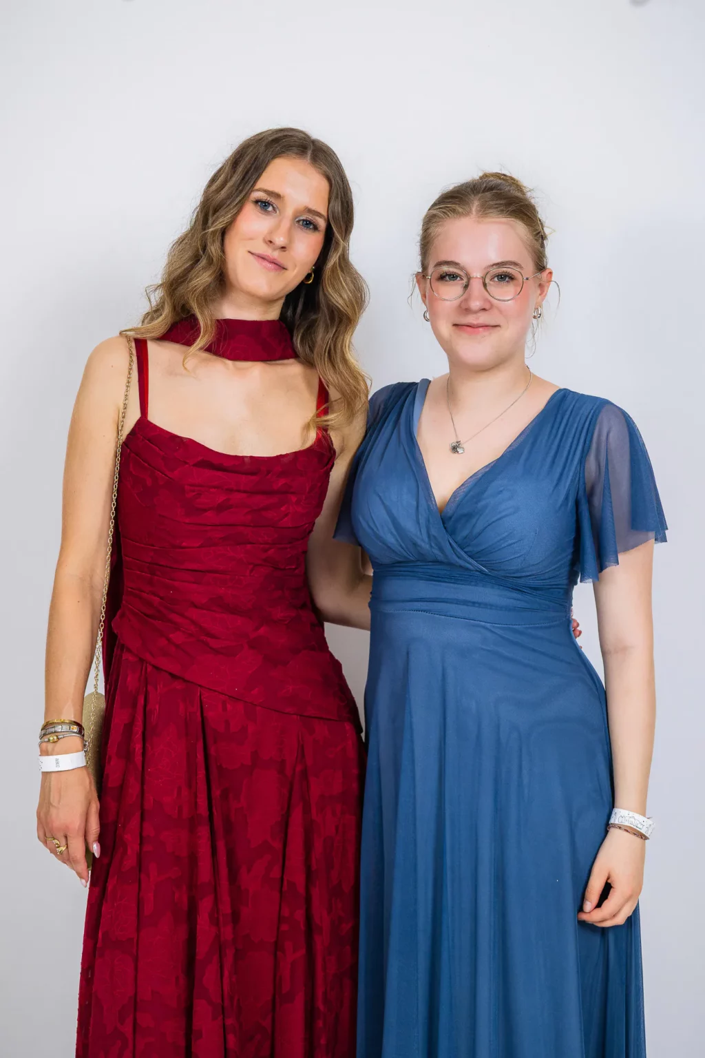 Fährhaus Kirschenland – Zwei Abiturientinnen in eleganten Abendkleidern in Rot und Blau posieren vor einem weißen Hintergrund bei einem Abiball in Stade. | Jannes Romund Fotografie