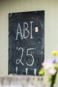 Abiballfotograf Stade – Eine Tafel mit der Aufschrift ABI '25 und einem kleinen Bild, umgeben von bunten Blumen. | Jannes Romund Fotografie