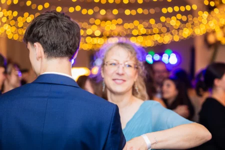 Fährhaus Kirschenland – Ein junger Mann im blauen Anzug tanzt mit einer Frau auf einem Abiball, umrahmt von einer stimmungsvollen Lichterkette im Hintergrund. | Jannes Romund Fotografie
