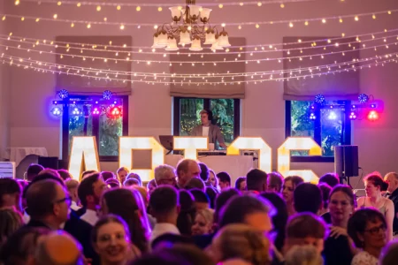 Fährhaus Kirschenland – DJ am Pult vor leuchtenden Buchstaben bei einem Abiball in Stade, umgeben von tanzenden Gästen unter einer Lichterkette im festlichen Saal. | Jannes Romund Fotografie