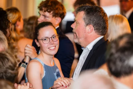 Fährhaus Kirschenland – Eine junge Frau mit Brille und ein Mann tanzen gemeinsam auf einem festlichen Abiball in Stade inmitten weiterer tanzender Gäste. | Jannes Romund Fotografie