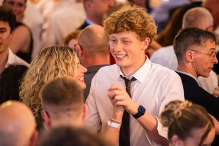 Fährhaus Kirschenland – Ein junger Abiturient mit lockigem Haar tanzt lächelnd mit einer Frau auf einem festlichen Abiball in Stade inmitten der tanzenden Gäste. | Jannes Romund Fotografie