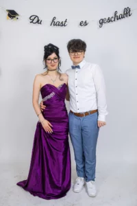 Fährhaus Kirschenland – Ein junges Paar in festlicher Kleidung posiert vor einem weißen Hintergrund mit dem Schriftzug Du hast es geschafft bei einem Abiball in Stade. | Jannes Romund Fotografie
