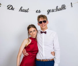 Fährhaus Kirschenland – Ein Paar in festlicher Kleidung posiert vor einem weißen Hintergrund mit dem Schriftzug Du hast es geschafft bei einem Abiball in Stade. | Jannes Romund Fotografie