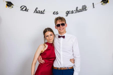 Fährhaus Kirschenland – Ein Paar in festlicher Kleidung posiert vor einem weißen Hintergrund mit dem Schriftzug Du hast es geschafft bei einem Abiball in Stade. | Jannes Romund Fotografie