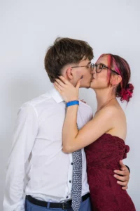 Fährhaus Kirschenland – Ein junges Paar küsst sich vor einem weißen Hintergrund im mobilen Fotostudio bei einem Abiball in Stade, festlich gekleidet in Hemd und Abendkleid. | Jannes Romund Fotografie