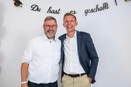 Fährhaus Kirschenland – Zwei fröhliche Männer im mobilen Fotostudio beim Abiball vor einem weißen Hintergrund mit dem Schriftzug Du hast es geschafft. | Jannes Romund Fotografie