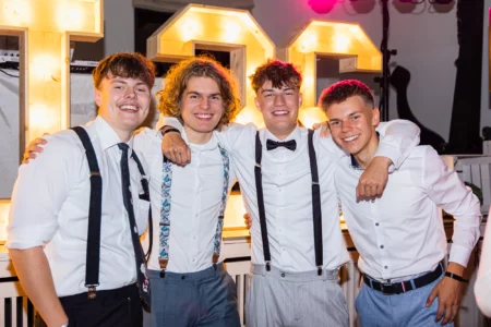 Fährhaus Kirschenland – Vier fröhliche Abiturienten in festlicher Kleidung mit Hosenträgern vor leuchtenden Zahlen bei einem Abiball in Stade. | Jannes Romund Fotografie