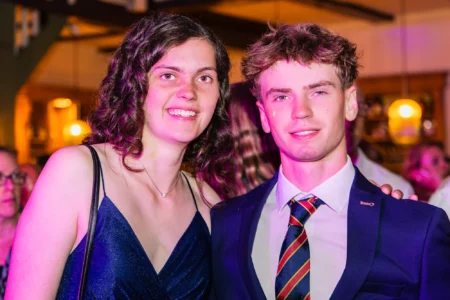 Fährhaus Kirschenland – Ein junges Paar in festlicher Kleidung lächelt bei einem Abiball in Stade in die Kamera, beleuchtet durch stimmungsvolles, violettes Partylicht. | Jannes Romund Fotografie