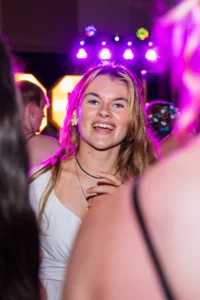 Fährhaus Kirschenland – Eine fröhliche Abiturientin lacht bei einer Abiball Feier in Stade, umgeben von Partygästen und stimmungsvoller, violetter Beleuchtung. | Jannes Romund Fotografie