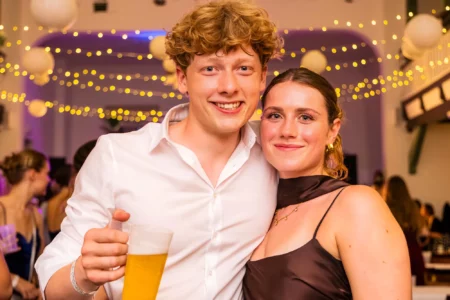 Fährhaus Kirschenland – Ein junges Paar lächelt in die Kamera auf einem Abiball in Stade, im Hintergrund stimmungsvolle Lichterketten und eine festliche Atmosphäre. | Jannes Romund Fotografie