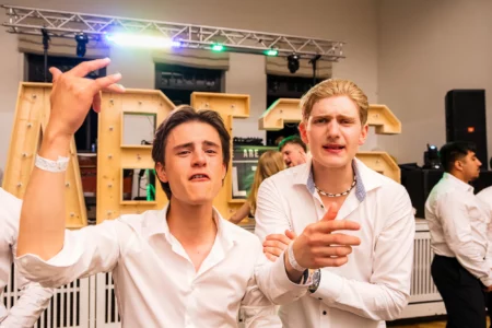 Fährhaus Kirschenland – Zwei Abiturienten in weißen Hemden feiern ausgelassen vor beleuchteten Holzbuchstaben auf einem Abiball in Stade mit DJ-Technik im Hintergrund. | Jannes Romund Fotografie