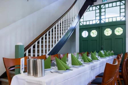 Fährhaus Kirschenland – Festlich gedeckte Tafel für einen Abiball mit grünen Servietten, Weingläsern und Sektkühlern vor einer historischen Treppe in einer Eventlocation. | Jannes Romund Fotografie