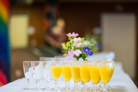 Abiballfotograf Stade – Eine Reihe von Gläsern mit orangefarbenem Getränk und einer Blumenvase auf einem Tisch. | Jannes Romund Fotografie