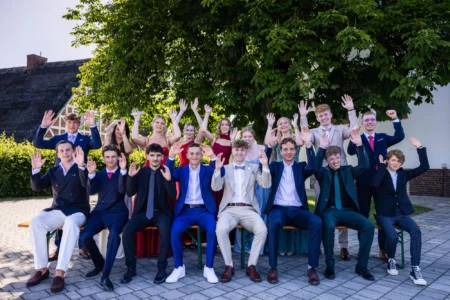 Abiballfotograf Stade – Eine Gruppe junger Menschen in festlicher Kleidung posiert fröhlich im Freien und hebt die Hände. | Jannes Romund Fotografie