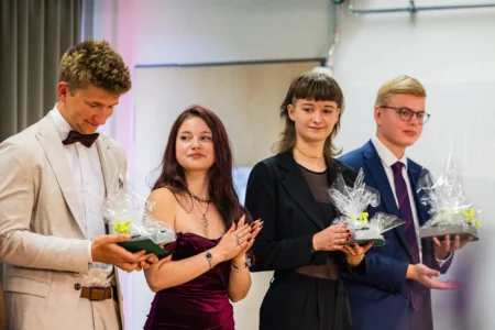Abiballfotograf Stade – Vier junge Erwachsene stehen auf einer Bühne und halten Geschenke in den Händen, während sie applaudieren. | Jannes Romund Fotografie